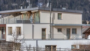 A two-story building with a balcony, a staircase, and a view of a mountainous area.