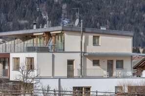 A two-story building with a balcony, a staircase, and a view of a mountainous area.