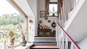 Een trap met een rode leuning die uitkomt op een plateau met een houten kast en wanddecoraties.