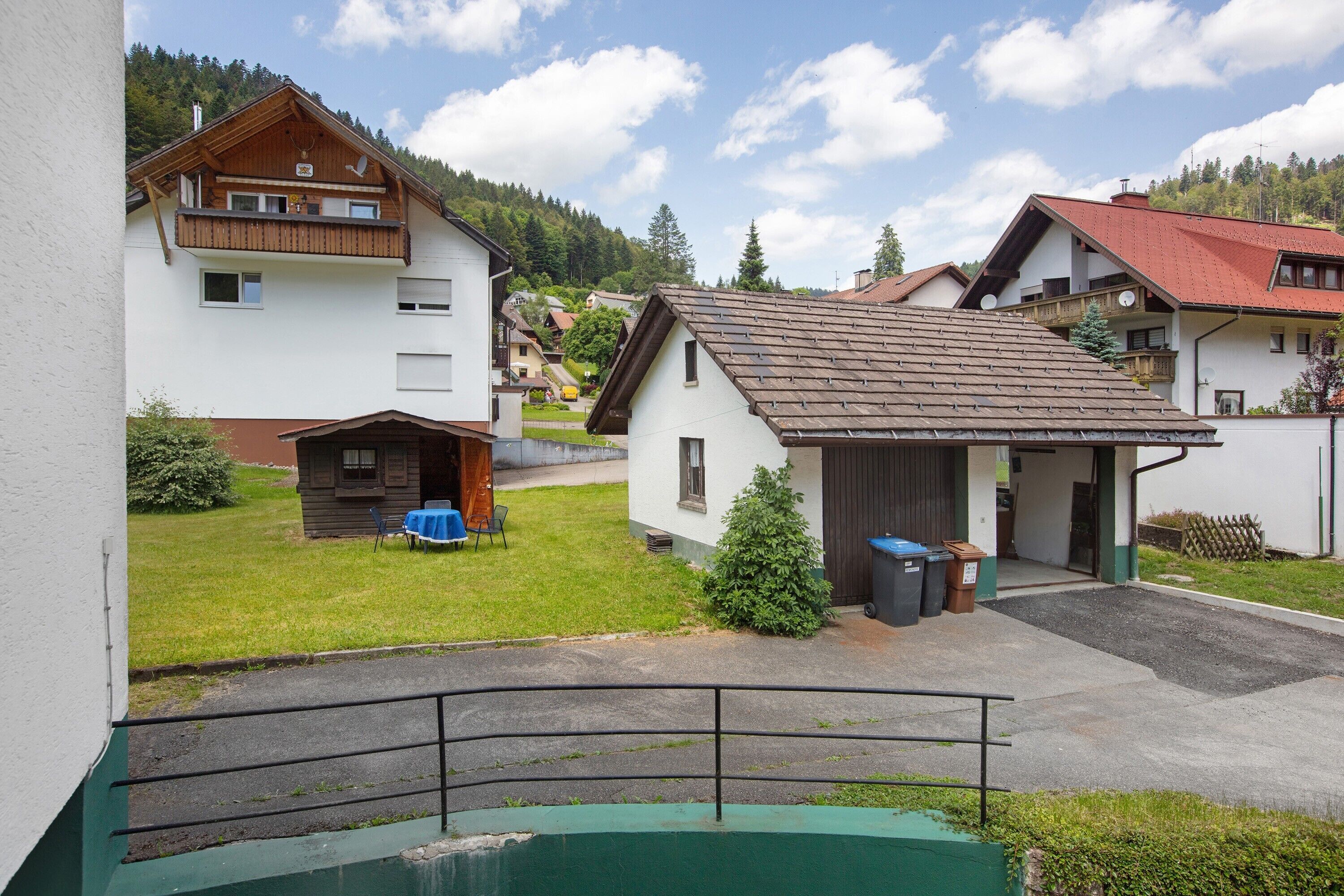 A residential area with houses, a small building with a garage, and a green swimming pool.