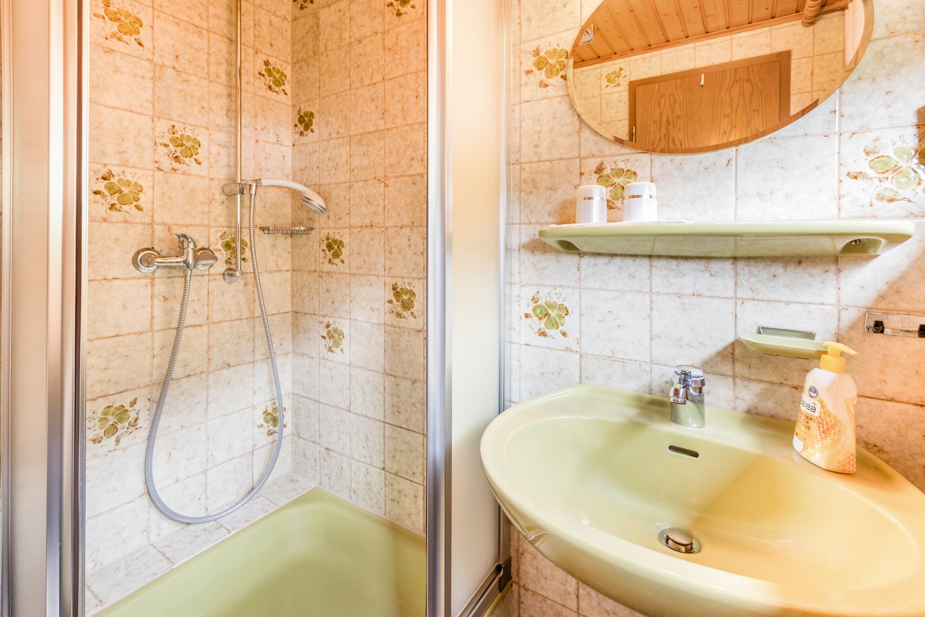 A bathroom with a shower, a sink, a mirror, and a shelf with toiletries.