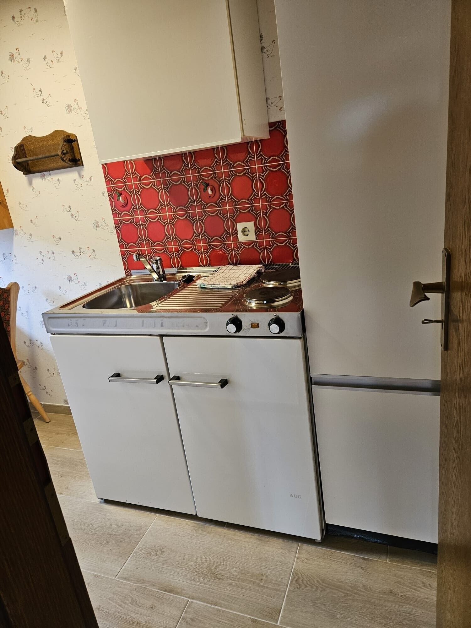 A kitchen with a white stove, a red patterned backsplash, and a white refrigerator.