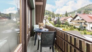 A balcony with a table and chairs, overlooking a residential area with houses and greenery. - Apartment "Am Wehrastrand 5" in a Spa Town in the Southern Black Forest with Mountain View (Todtmoos)