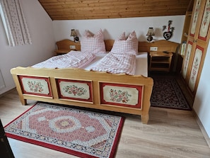 Une chambre à coucher avec un lit en bois, deux tables de chevet, une couvre-lit à carreaux rouges et blancs, un tapis à motifs et une armoire en bois.