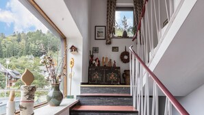 A staircase with a red handrail, a window with a view of trees, and a shelf with decorative items. - Apartment "Am Wehrastrand 5" in a Spa Town in the Southern Black Forest with Mountain View (Todtmoos)
