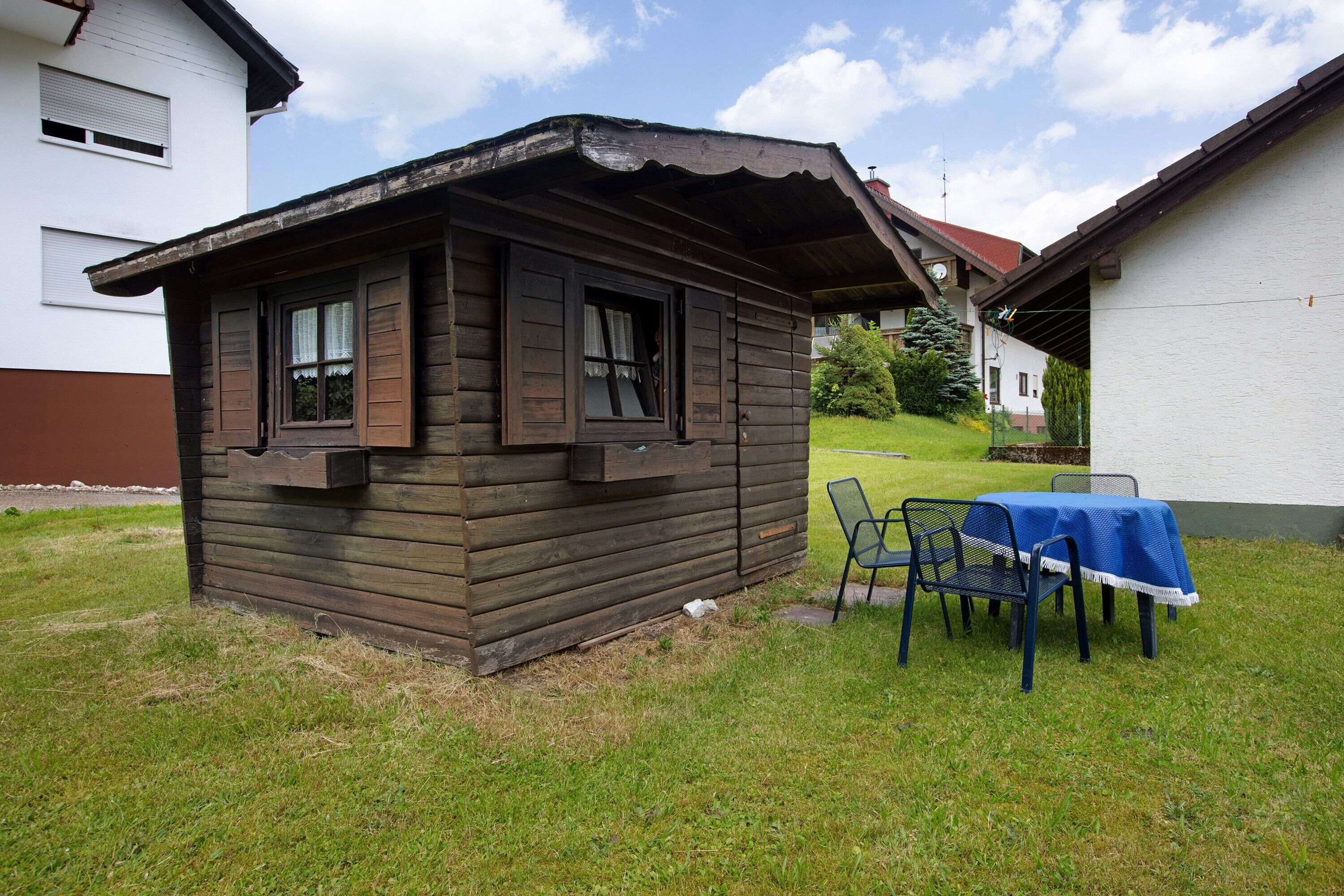 Une cabane en bois avec une petite véranda, une table avec des chaises et une nappe bleue.
