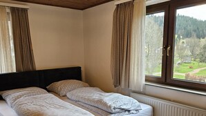Ein Schlafzimmer mit Bett, Holzboden, Fenster mit Vorhängen und Blick auf eine grüne Landschaft.