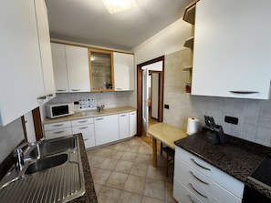 A modern kitchen with white cabinets, a stainless steel sink, a microwave, and a wooden countertop.
