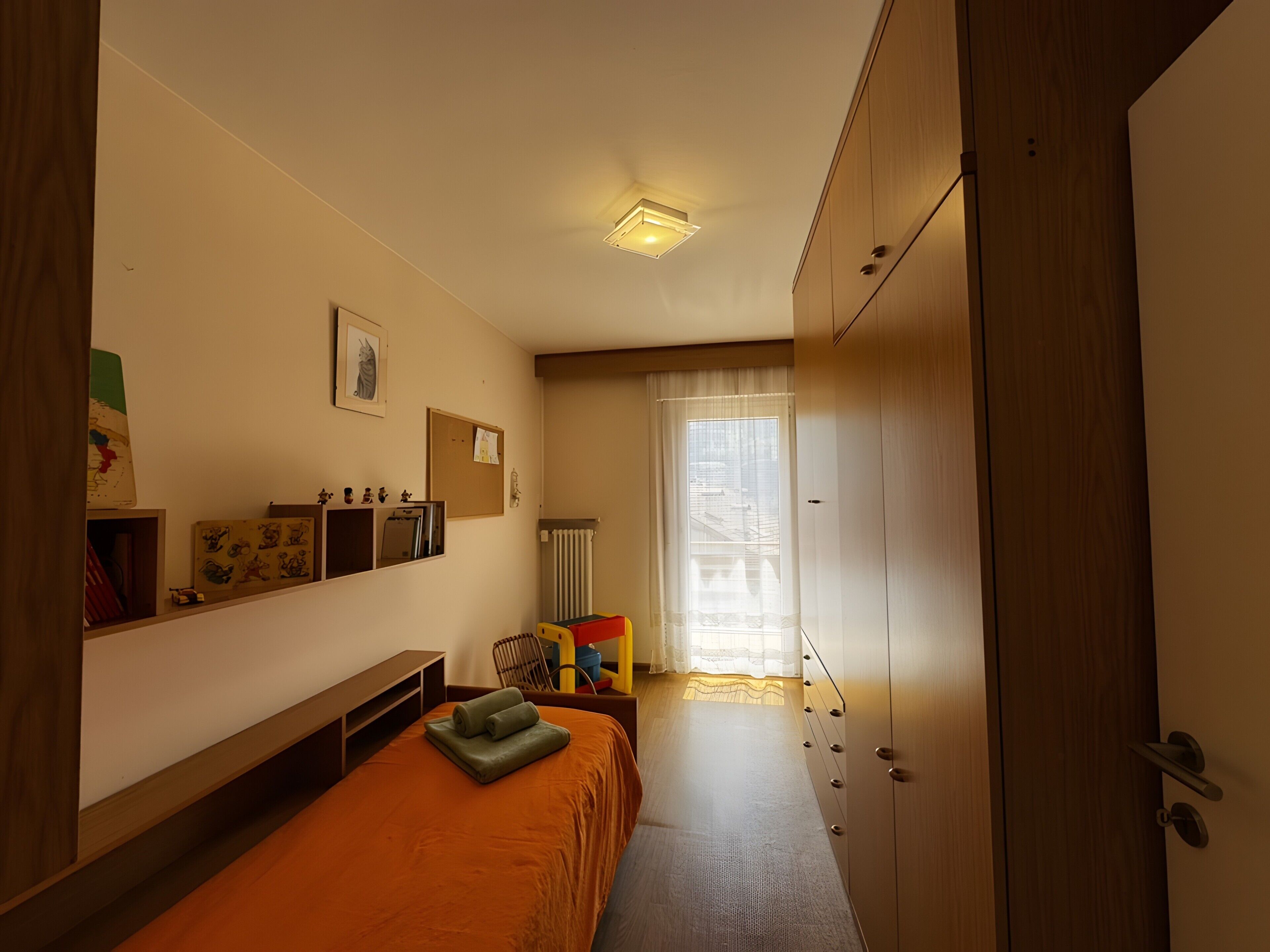 A bedroom with a bed, a wardrobe, a desk, and a chair.