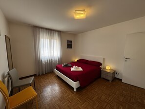 Hotellihuone, jossa on sänky, tuoli, yöpöytä ja pieni sivupöytä.