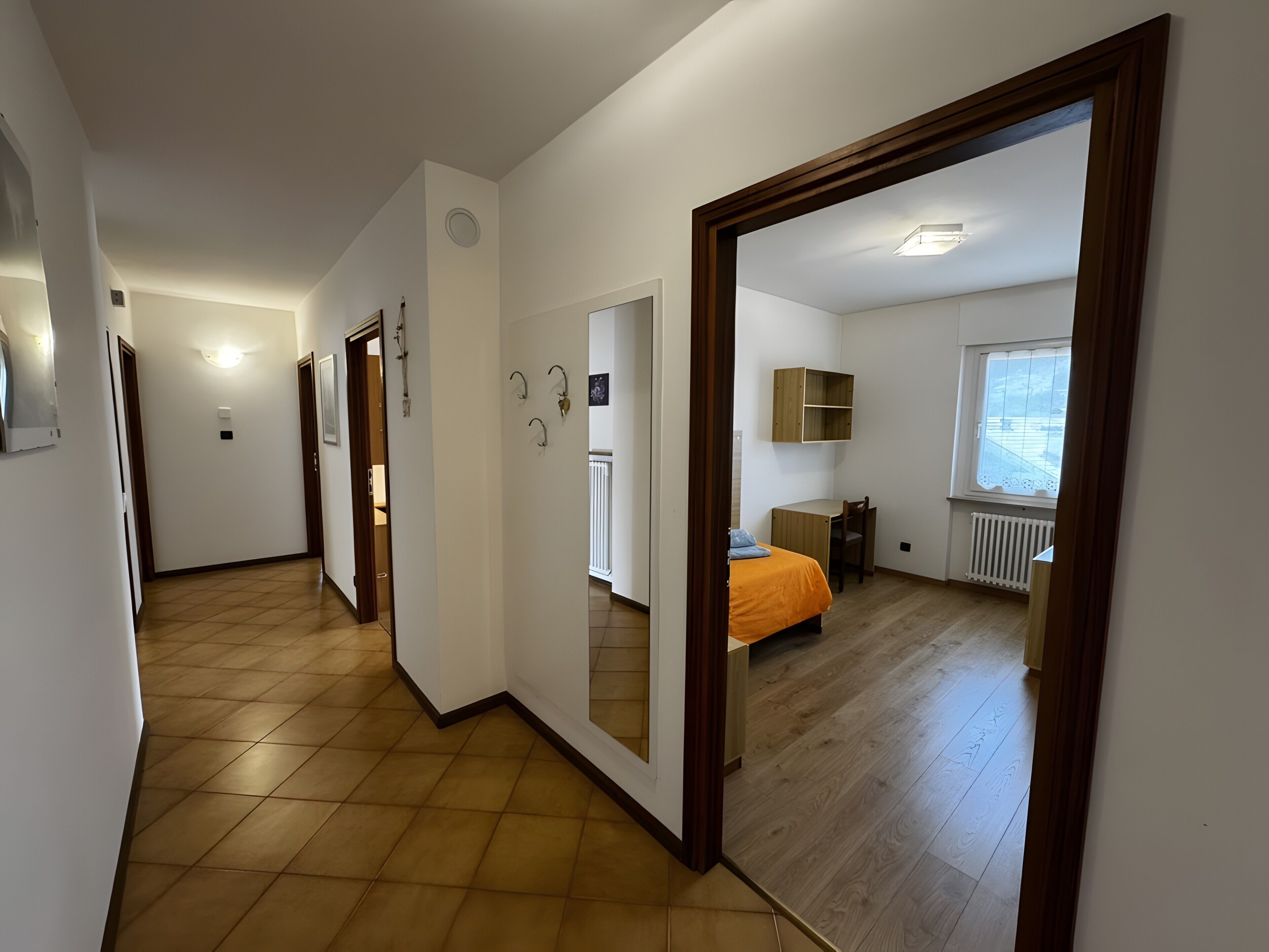 Ein Flur, der in ein Schlafzimmer mit einem Bett, einem Schreibtisch und einem Heizkörper führt.