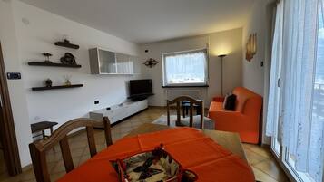 Sala de estar moderna com sofá, televisão e área de jantar com mesa e cadeiras.
