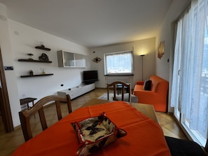 A modern living room with a sofa, a TV, and a dining area with a table and chairs.
