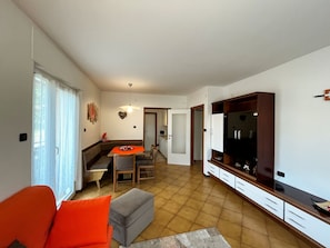 Un soggiorno con zona pranzo, televisore e cucina sullo sfondo.