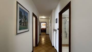 A hallway with a framed picture on the left, a shower area on the right, and a dining area in the background.