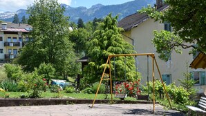 A park with a swing set, a bench, and a building with a sloped roof. - Child-friendly Holiday Apartment "Cornon" with Mountain View, Sun Terrace & Wi-Fi (Tesero)