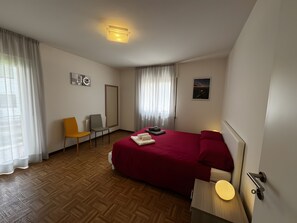 Habitación de hotel con cama, una silla, un escritorio, un espejo y una ventana con cortinas.