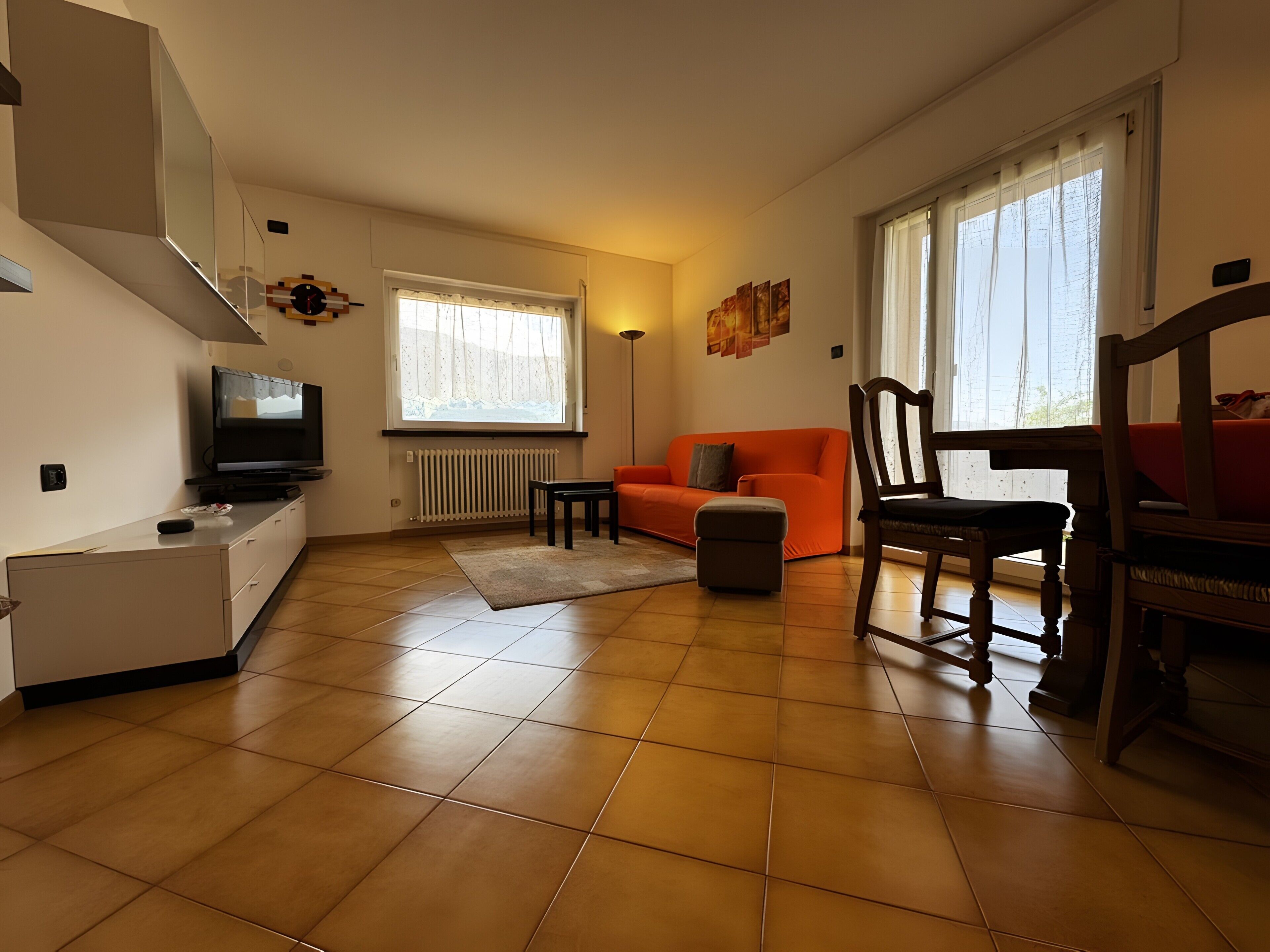 Una sala de estar con un sofá, un televisor, una mesa de comedor con sillas y un radiador.