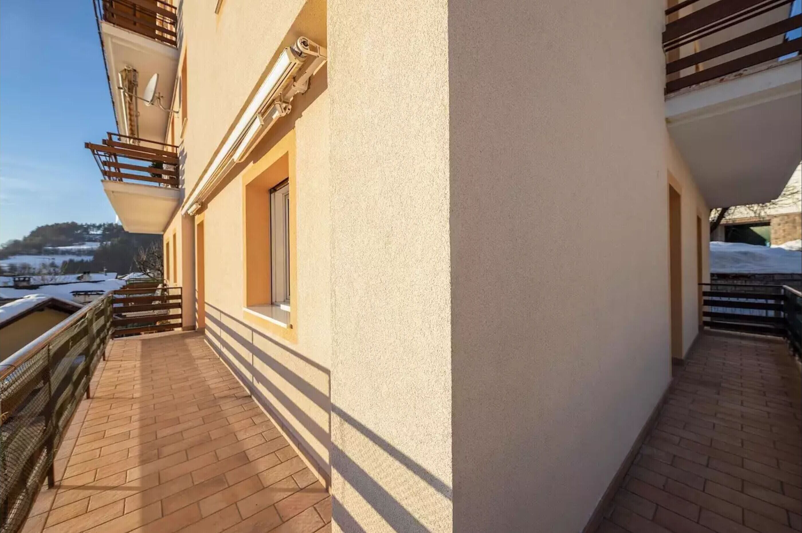 Un balcone con vista su un paesaggio innevato, un edificio dalla facciata beige e un cielo sereno.