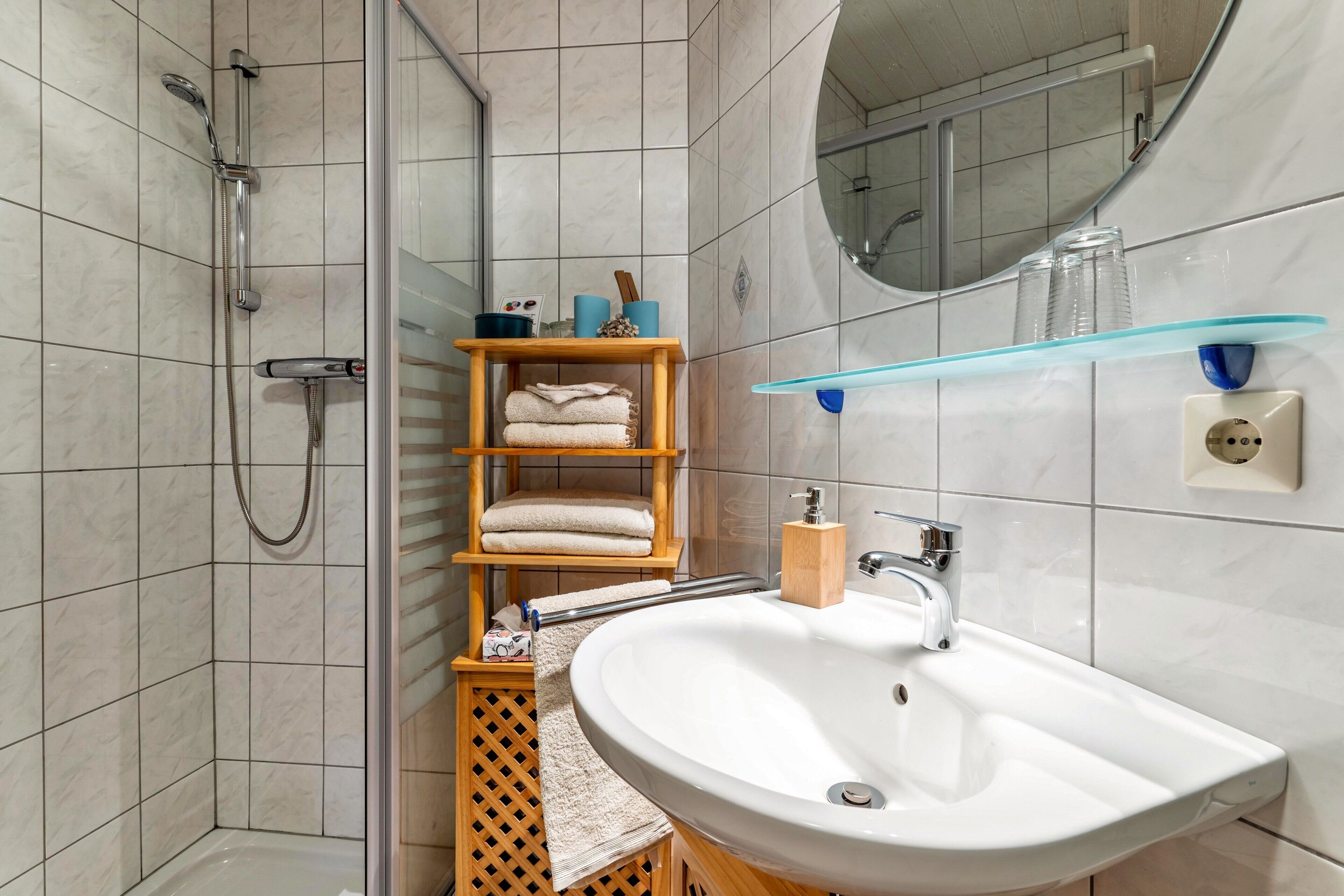 Kylpyhuone, jossa on suihku, pesuallas, peili ja hylly, jossa on hygieniatuotteita.