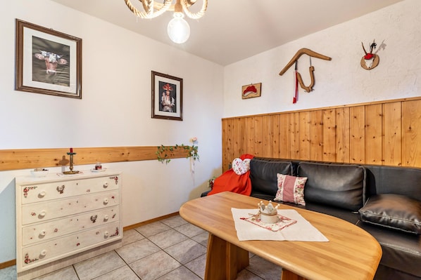 A room with a wooden dresser, a black leather sofa, a wooden table, and wall-mounted decorations.