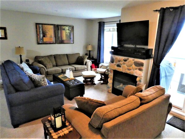A living room with a sofa, armchairs, a fireplace, a television, and a window with curtains.