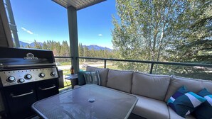 Een terras buiten met een barbecue, een bank en een tafel.