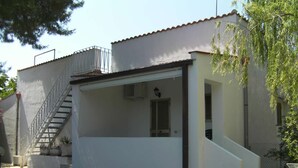 Un bâtiment blanc doté d’un patio couvert, d’un escalier en métal et d’une petite fenêtre.