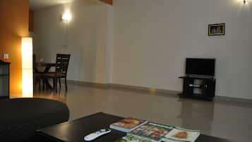 Un salon comprenant un canapé, une table basse avec des magazines, un meuble pour la télévision et un ventilateur de plafond.