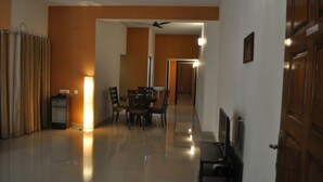 A spacious living area with a dining table and chairs, a ceiling fan, and a door leading to another room. - Jyothi Suites (Tiruchirappalli)