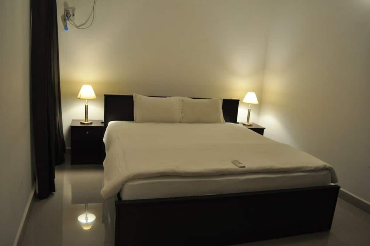 Ein ordentlich bezogenes Bett mit Fernbedienung, zwei Nachttischlampen und einem schwarzen Nachttisch.
