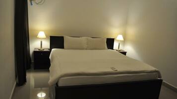 A neatly made bed with a remote control, two bedside lamps, and a black nightstand.