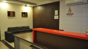 A reception area with a red counter, black leather sofa, and framed pictures on the wall. - Jyothi Suites (Tiruchirappalli)
