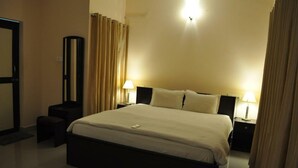 A neatly arranged hotel room with a large bed, two bedside tables with lamps, a mirror, and a door. - Jyothi Suites (Tiruchirappalli)