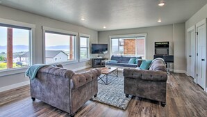 A spacious living room with a large window, a flat-screen TV, a gray sofa, and a coffee table. - Lake-View Escape w/ Private Beach Resort Access! (Garden City)