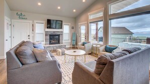A spacious living room with a fireplace, comfortable seating, and large windows offering a view of the landscape. - Lake-View Escape w/ Private Beach Resort Access! (Garden City)