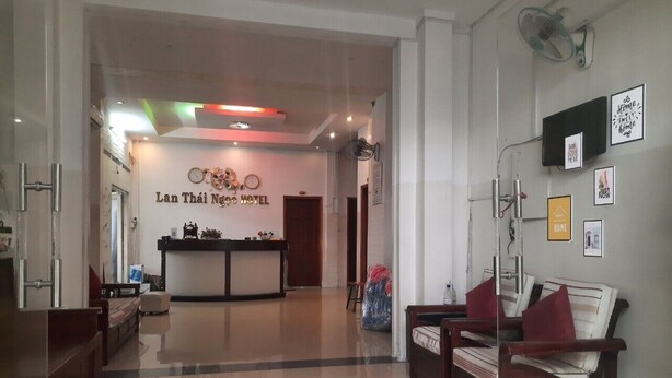 A hotel lobby with a reception desk, seating area, and a wall with framed pictures. - Lan Thai Ngoc (Cao Lanh)