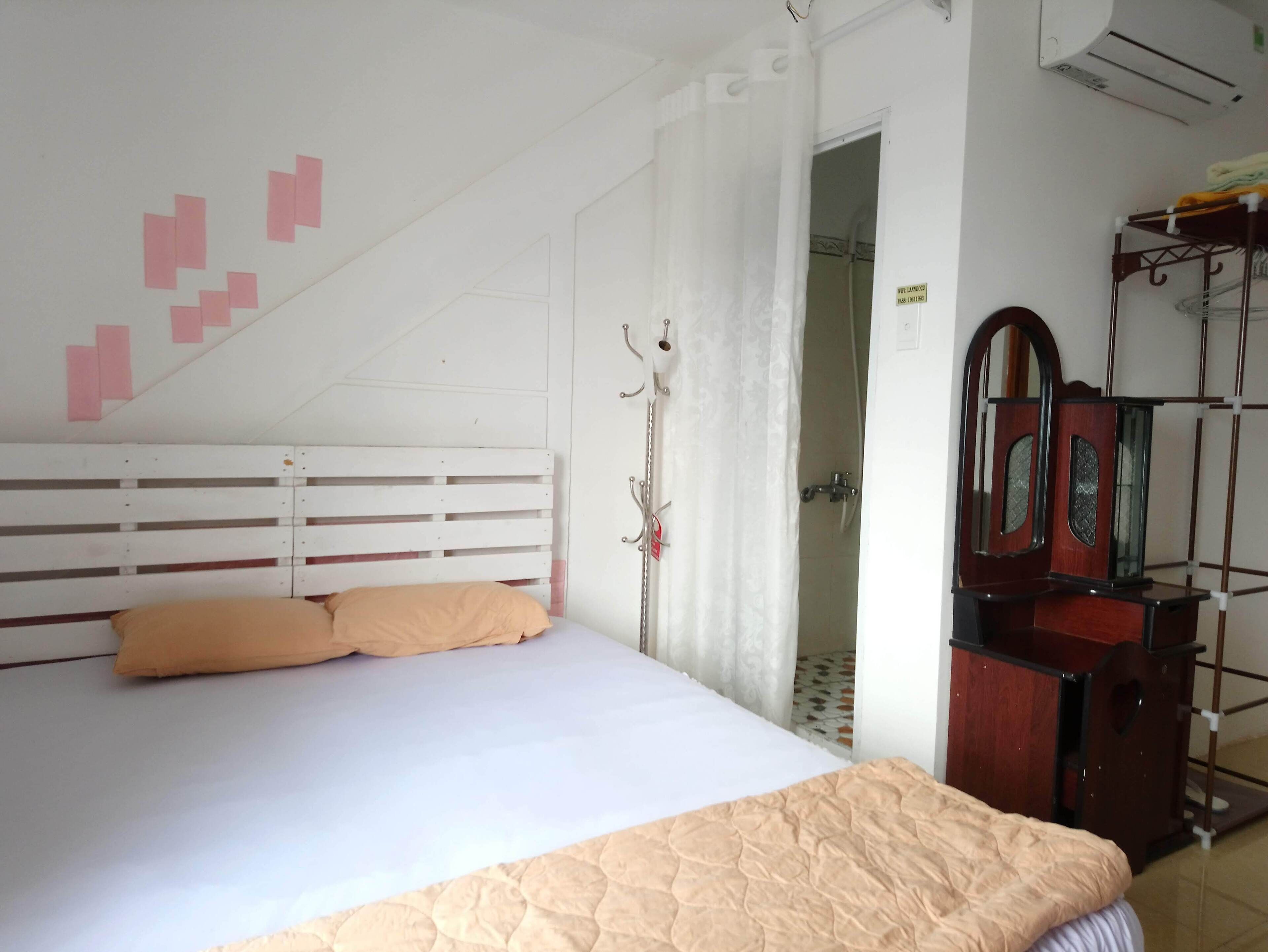 A bedroom with a bed, a wooden dresser, a mirror, and a shower area.