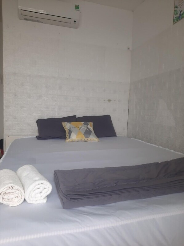 A hotel room with a bed, pillows, a folded blanket, rolled towels, and an air conditioning unit on the wall. - Lan Thai Ngoc (Cao Lanh)