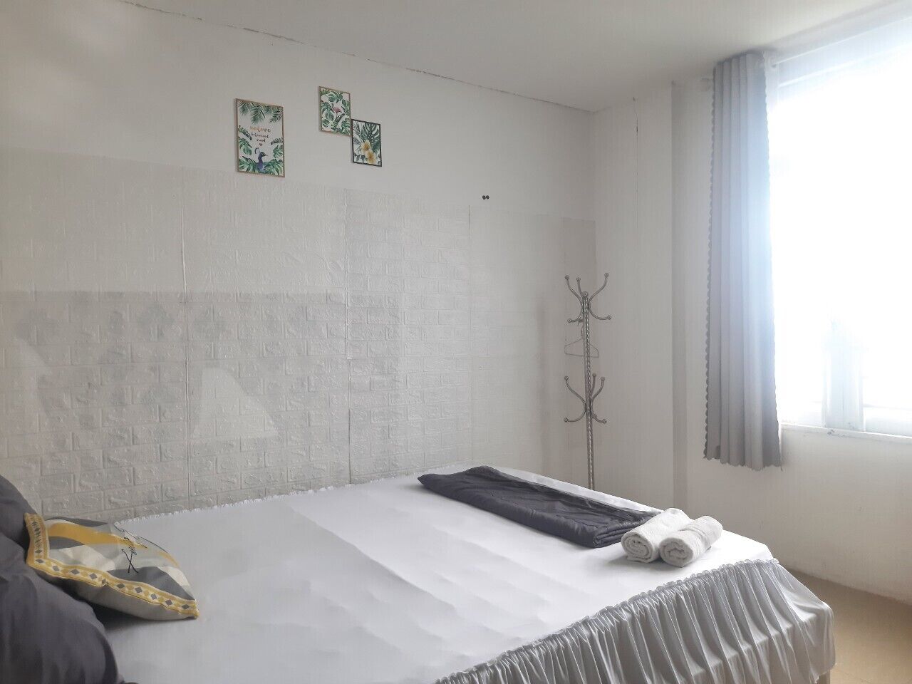 Ett hotellrum med en säng, en klädställning och två små konstverk på väggen.