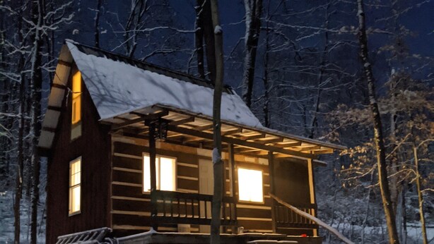 A wooden cabin with a snow-covered roof and a wooden staircase leading to the entrance. -  Hocking Hills,Cozy Secluded Cabin,Minutes to Caves/WiFi/Pet Friendly! (McArthur)