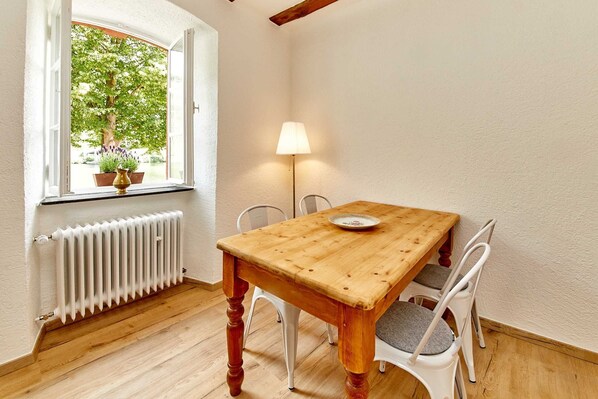 A dining area with a wooden table and white chairs, a window with a view of greenery, and a floor heater.