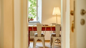 Un comedor con una mesa de madera y sillas blancas, una ventana con vistas a la vegetación y una lámpara sobre la mesa.