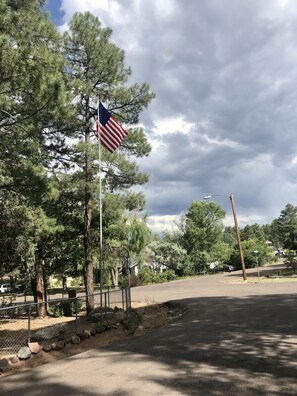 A flagpole with an American flag, surrounded by trees and a paved road. - Mountain Retreat a property in the cool pines of Show Low, AZ.  (Show Low)
