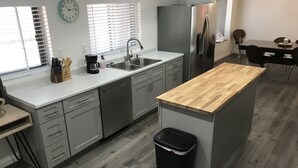 Eine moderne Küche mit grauen Schränken, einem Edelstahlkühlschrank, einer Holztischinsel und einer schwarzen Mülltonne.