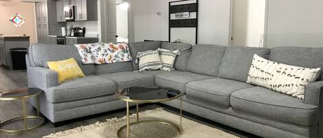 A modern living room with a grey sectional sofa, a small round coffee table, and a beige rug.