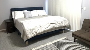 Ein Schlafzimmer mit einem Bett, einem Nachttisch, einem Sessel und einem Fenster mit Jalousien.