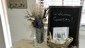 Ein Holztisch mit einem Willkommensschild, einem gerahmten Bild, einem Korb voller Snacks und einer Vase mit getrockneten Blumen.