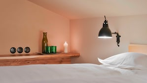 A bedroom with a wooden headboard, a bedside table with a green bottle, a white candle, and a black wall-mounted lamp.
