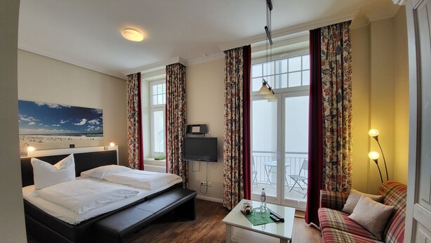 Ein Hotelzimmer mit Bett, Fernseher, Balkon und Sofa.